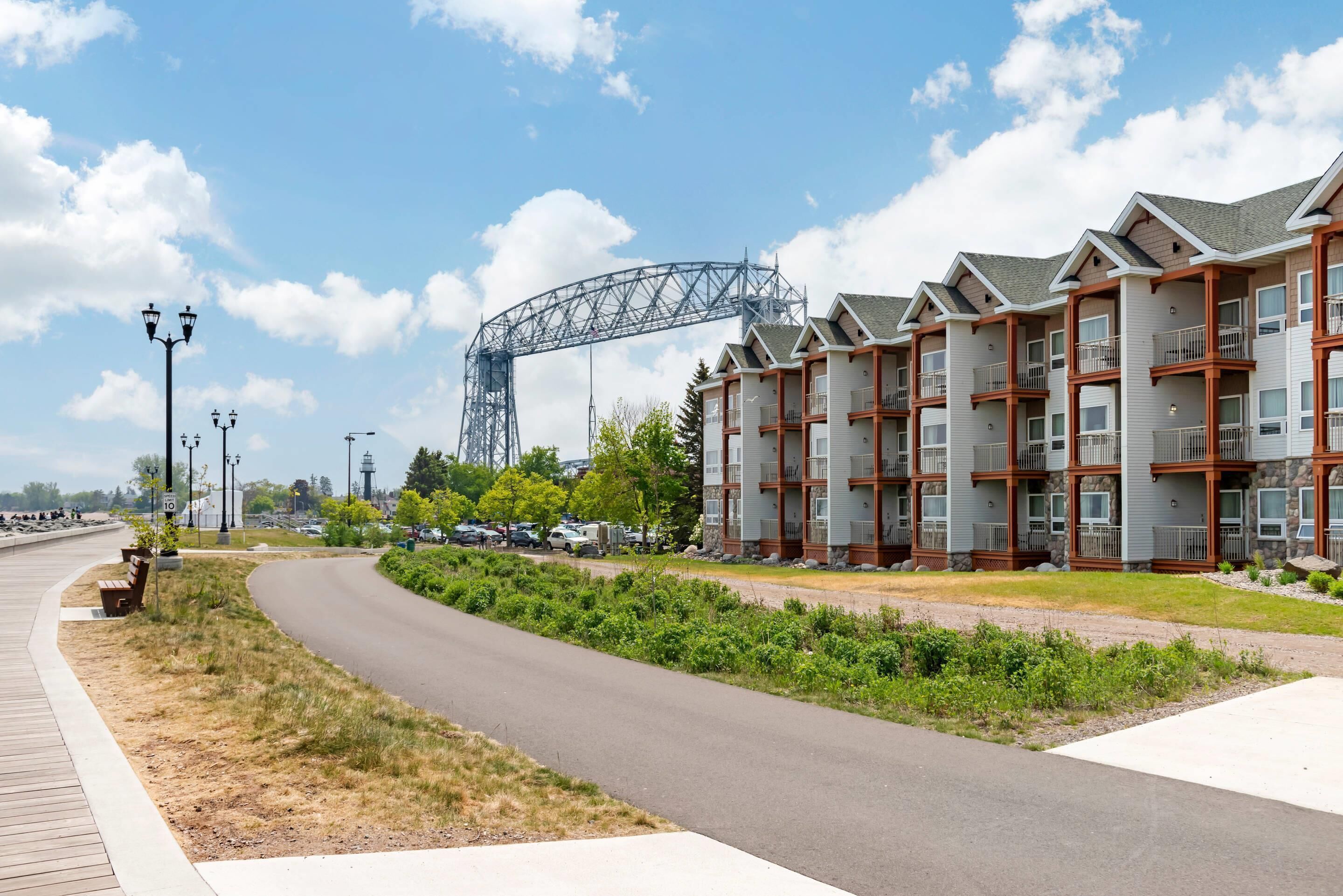 Een modern appartementencomplex met meerdere balkons, een bochtige weg en een grote metalen constructie op de achtergrond.