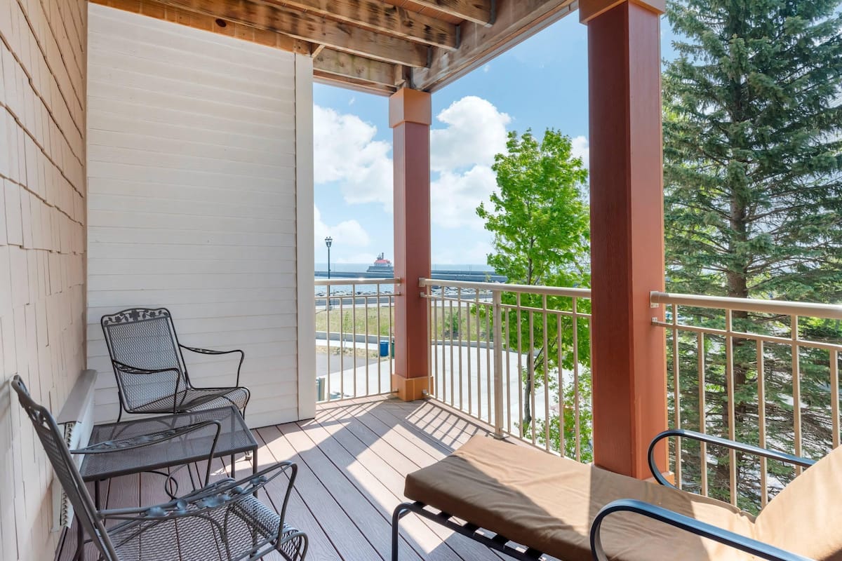 A covered outdoor area with a wooden deck, metal chairs, and a cushioned bench.