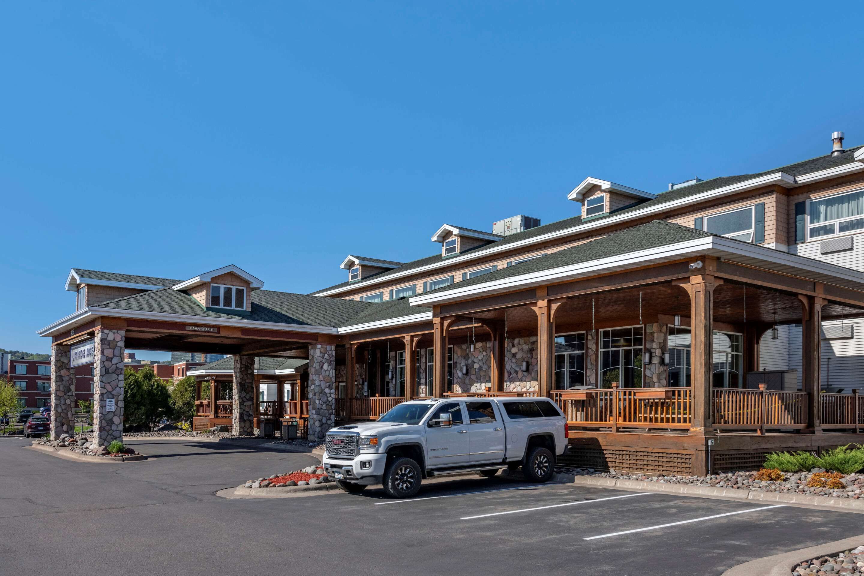 A hotel with a covered entrance, stone pillars, and a white SUV parked in front.
