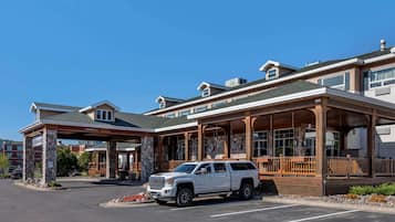 A hotel with a covered entrance, stone pillars, and a white SUV parked in front.