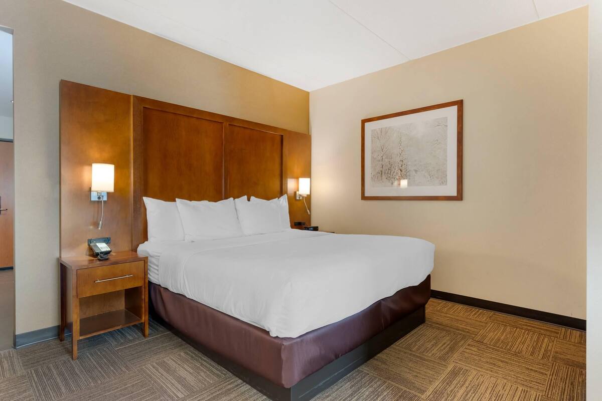 A hotel room with a large bed, wooden headboard, bedside lamps, a nightstand, and a framed picture on the wall.