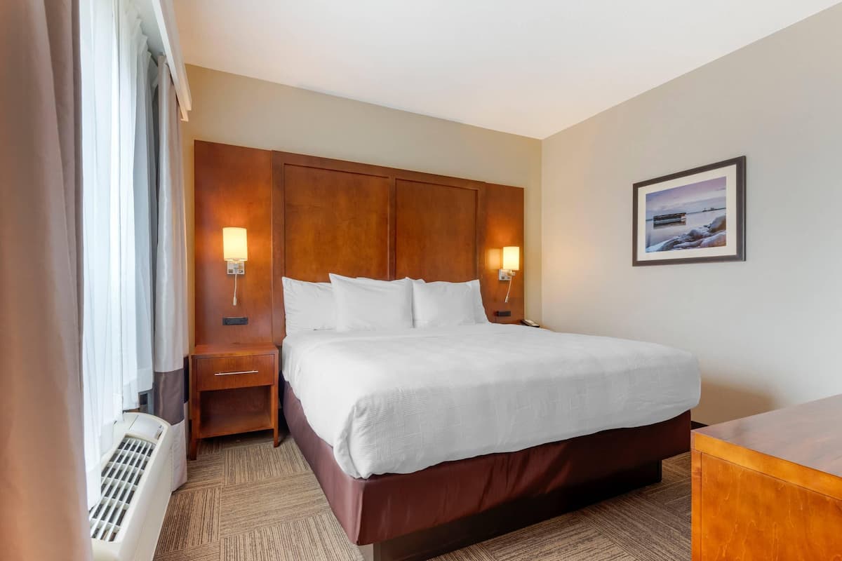 A hotel room with a large bed, wooden headboard, bedside lamps, a small nightstand, a heater, and a framed picture on the wall.