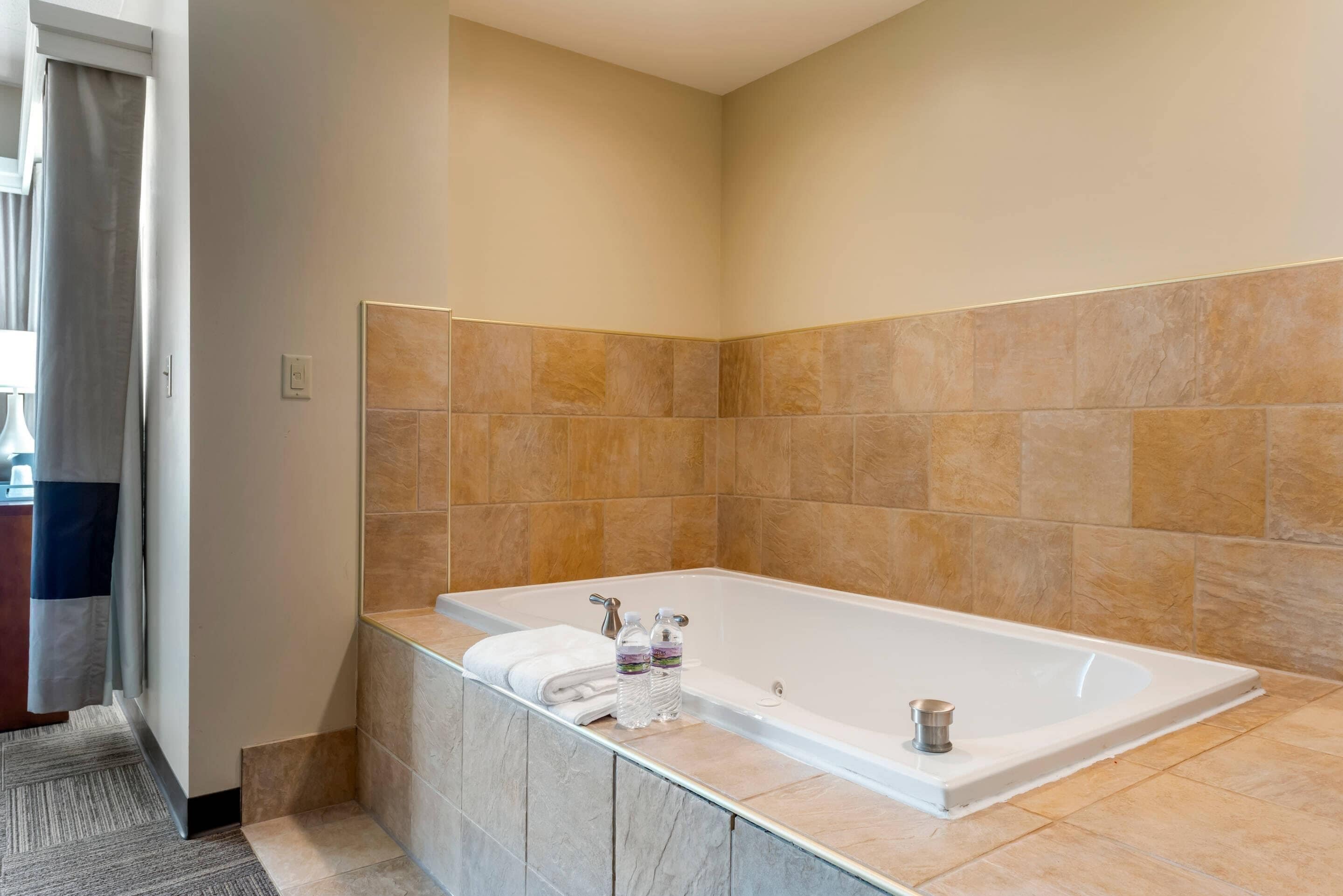 A modern bathroom with a large bathtub, marble countertops, and beige tiled walls.