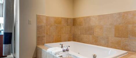 A modern bathroom with a large bathtub, marble countertops, and beige tiled walls.