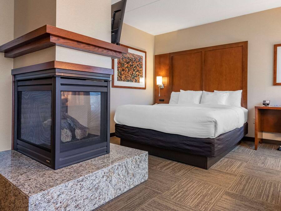 A hotel room with a bed, a fireplace, a wooden headboard, a nightstand, and a wall-mounted TV.