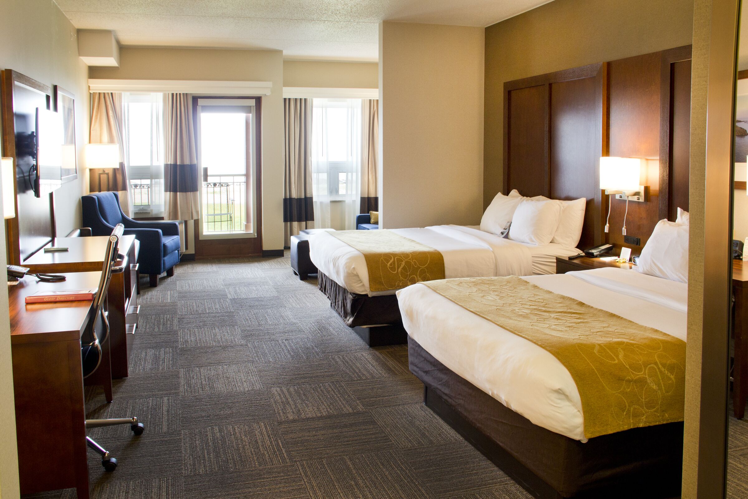 A hotel room with two beds, a desk, a chair, and a TV.