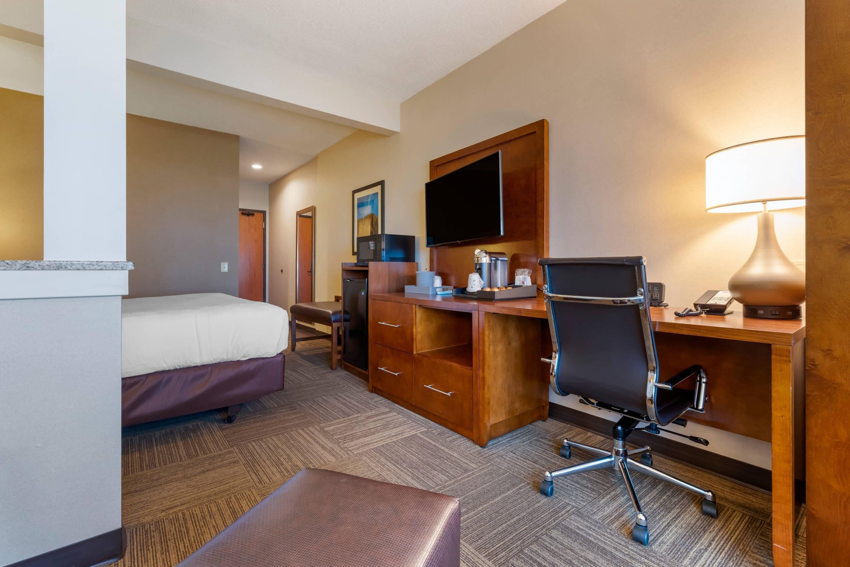 Habitación de hotel con cama, escritorio con computadora, silla, televisor y lámpara.