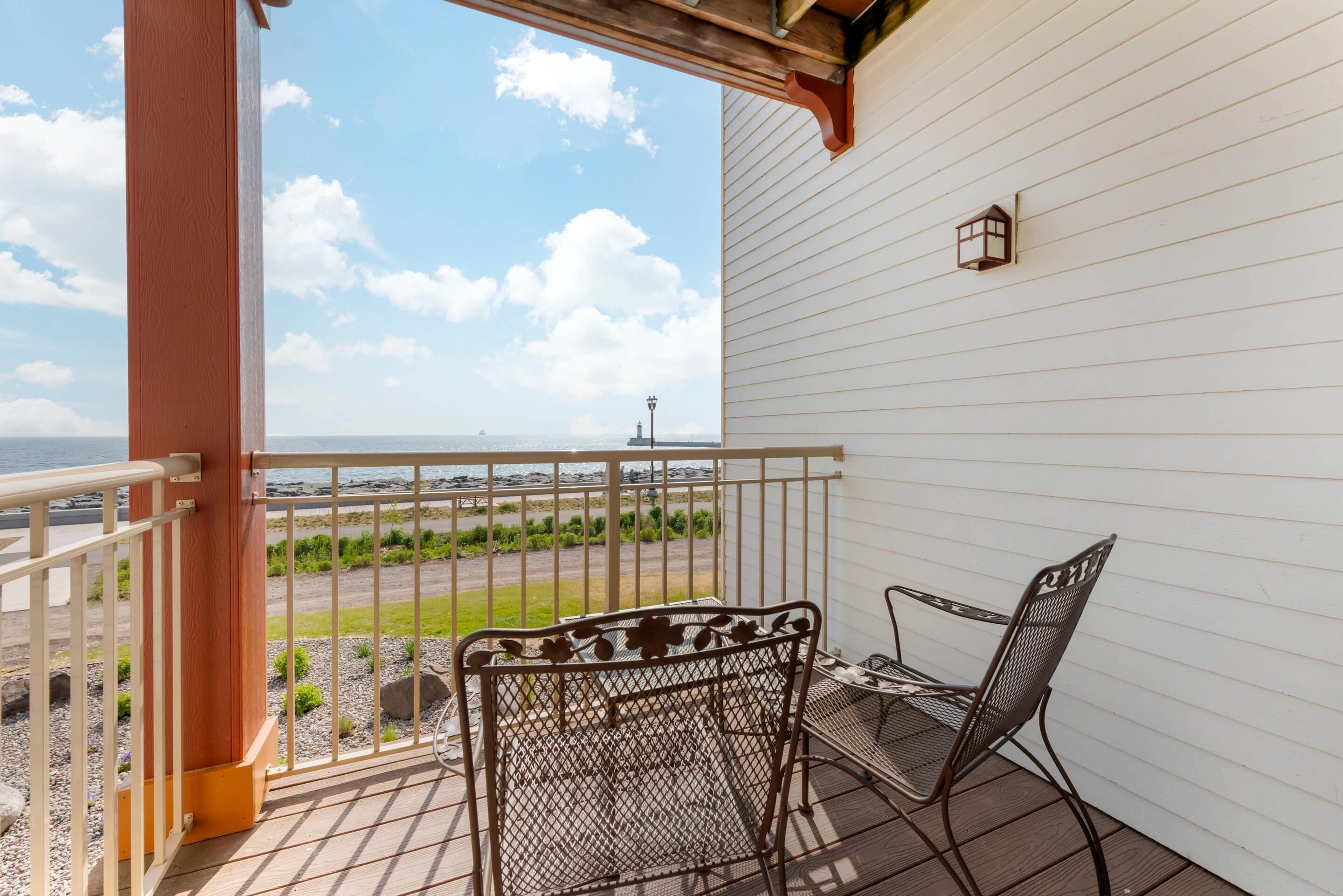 Een balkon met een metalen tafel en stoelen, met uitzicht op een gazon en een verafgelegen vuurtoren.
