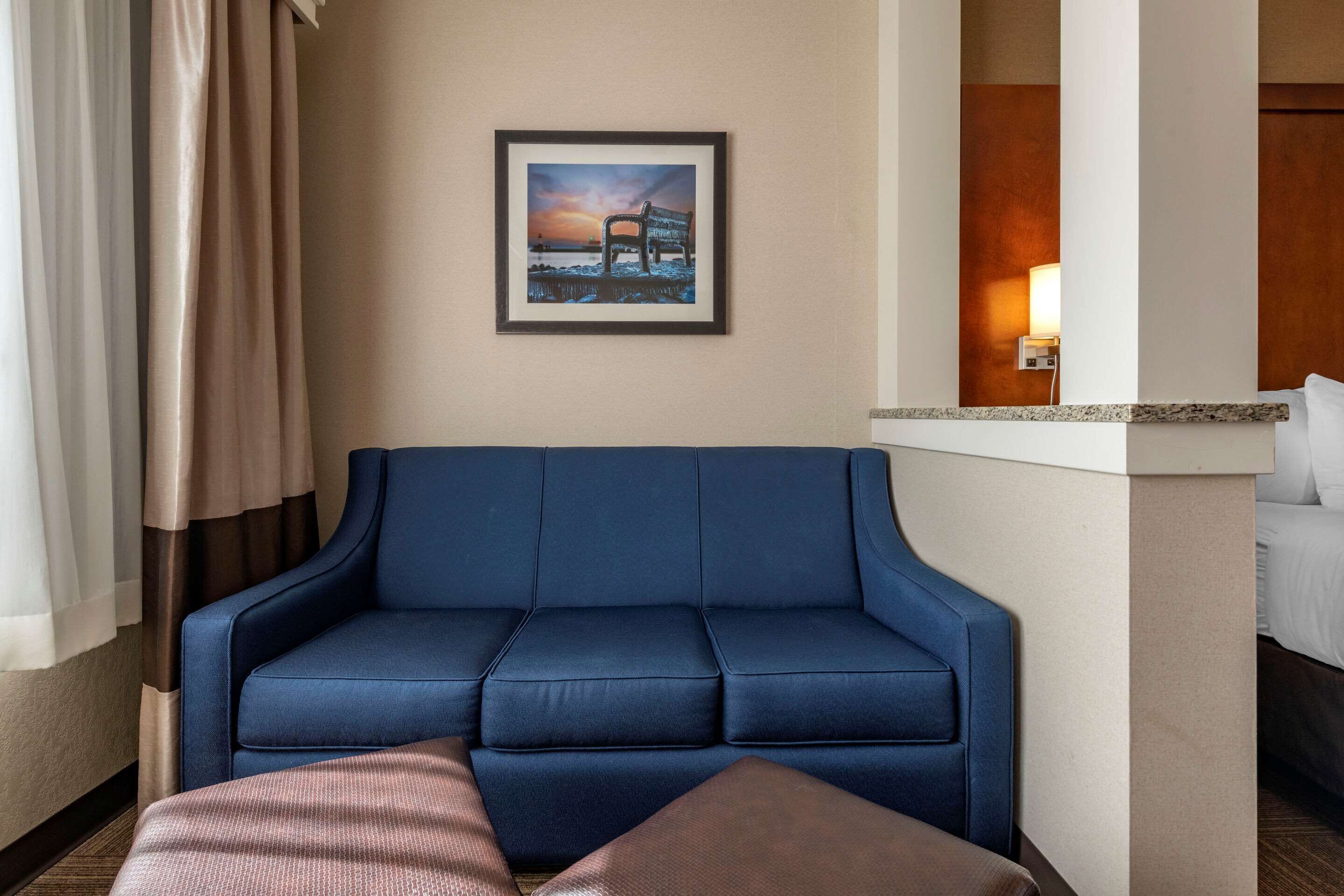 Une chambre d’hôtel avec un canapé bleu, un tableau encadré au mur et un lit avec du linge de maison blanc.