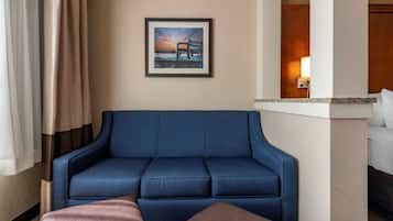 Une chambre d’hôtel avec un canapé bleu, un tableau encadré au mur et un lit avec du linge de maison blanc.