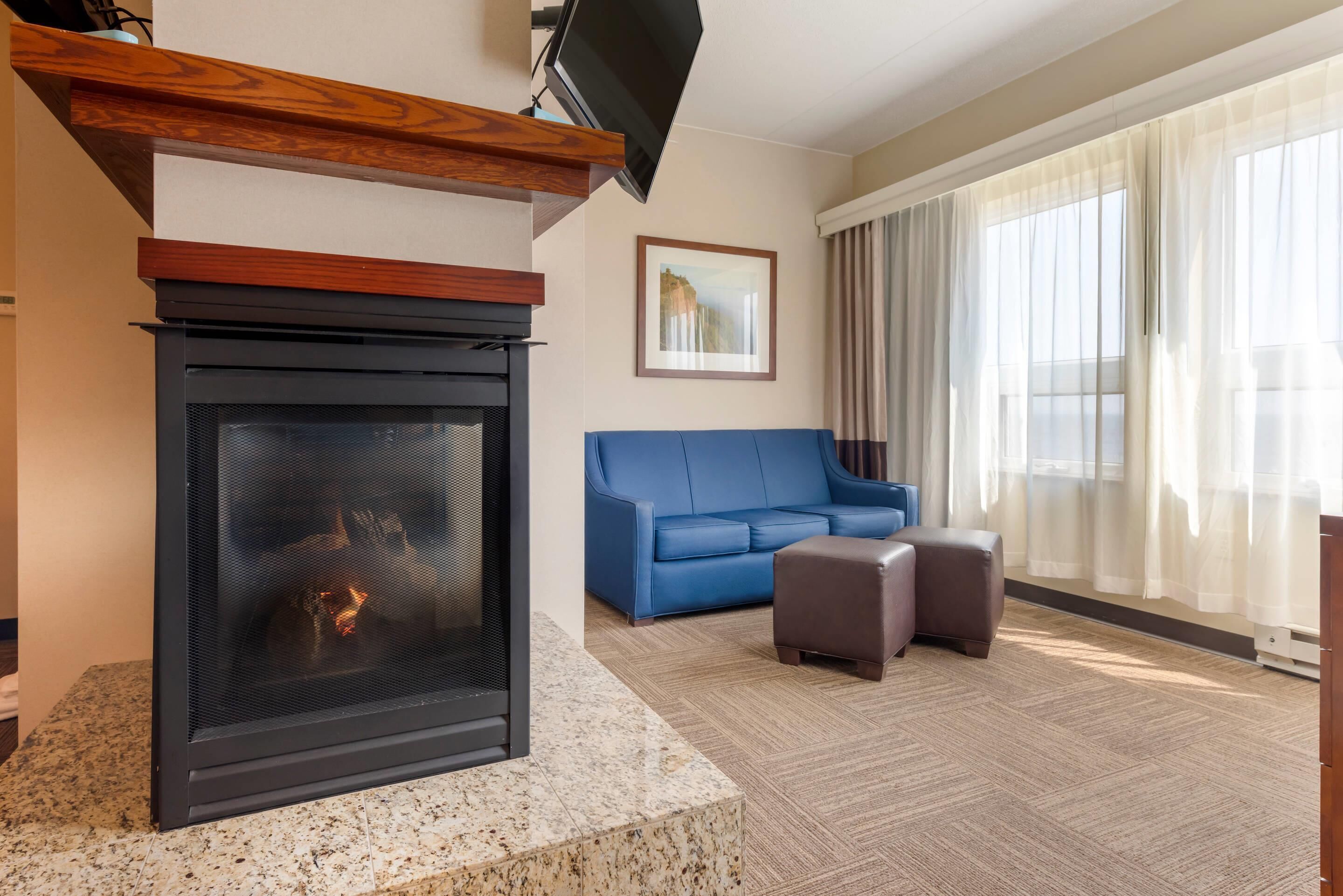 A modern living room with a fireplace, a blue sofa, and a large window with sheer curtains.