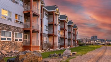 A row of multi-story buildings with balconies, a stone facade, and a gravel driveway.