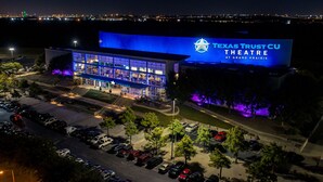 The Texas Trust CU Theatre at Grand Prairie, featuring a modern glass facade and a parking lot with several cars.