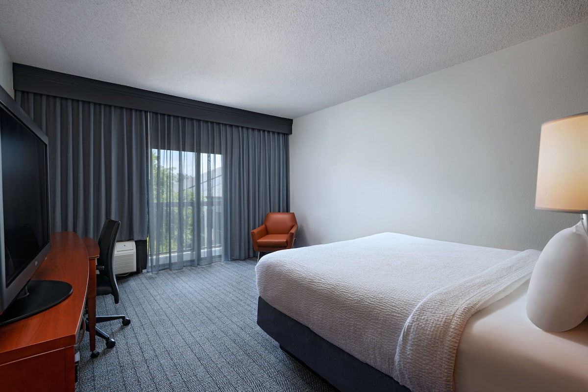Habitación de hotel con una cama grande, un escritorio con computadora, una silla y un televisor.