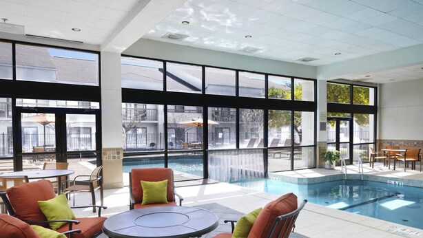 A pool area with orange chairs and a table, large windows, and a view of the outside.
