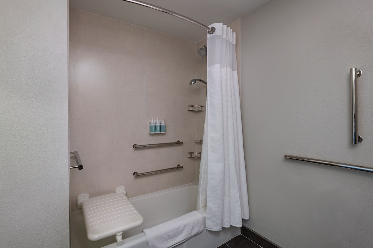 Un baño con ducha, barras de apoyo, inodoro y toallero.