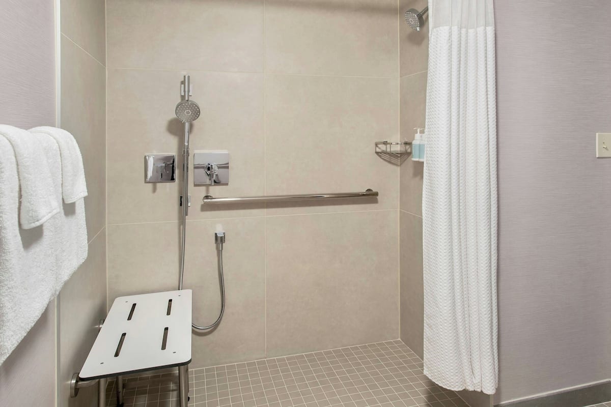 Un área de ducha con cabezal de ducha de mano, un perchero y un panel de control de la ducha.