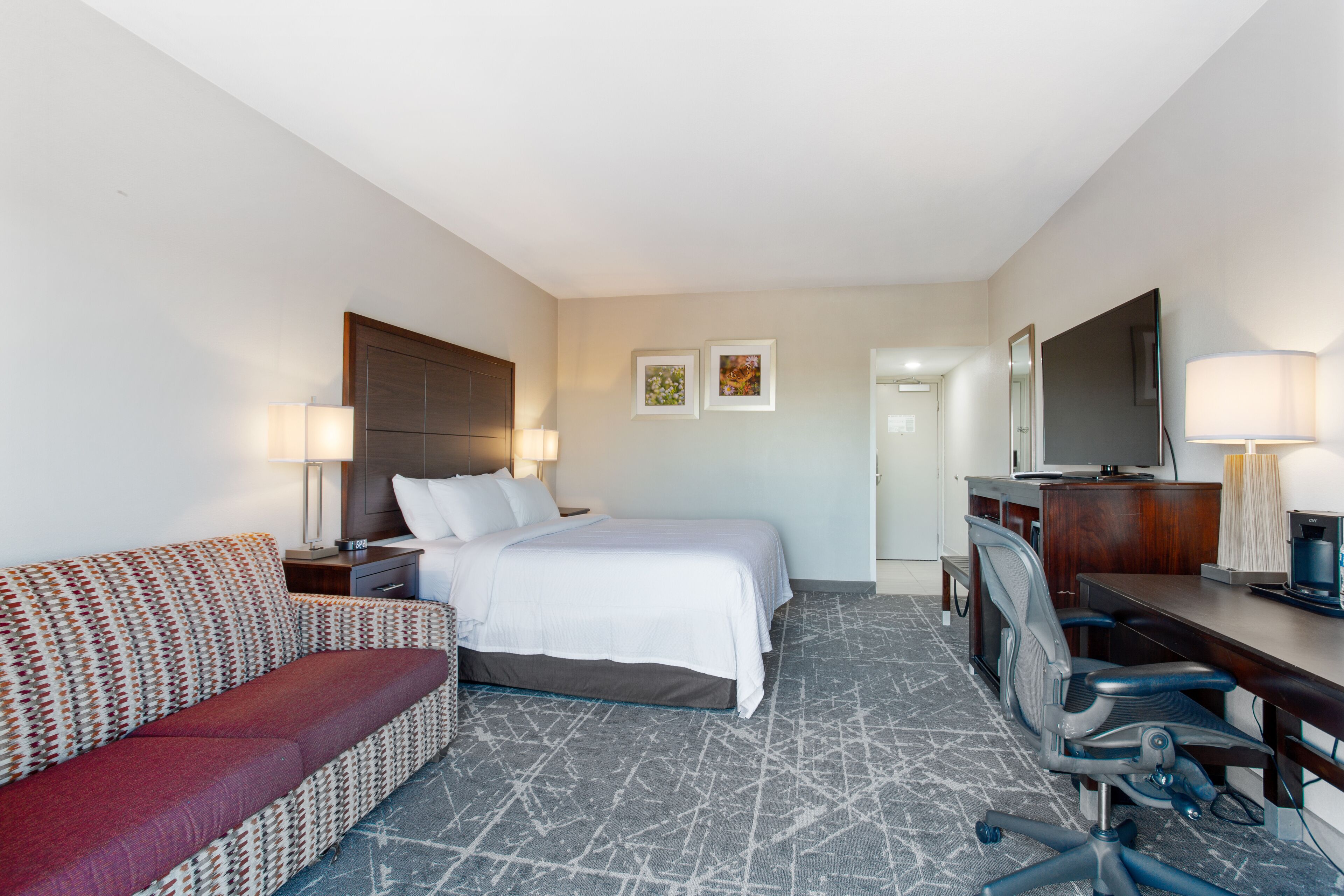 Habitación de hotel con cama, sofá, escritorio con silla, televisión y dos lámparas.