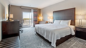 A hotel room with a large bed, a desk, a chair, and a view of the city.
