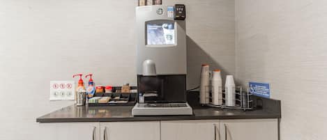 A coffee machine with a digital display, condiment dispensers, and a coffee cup holder on a counter.