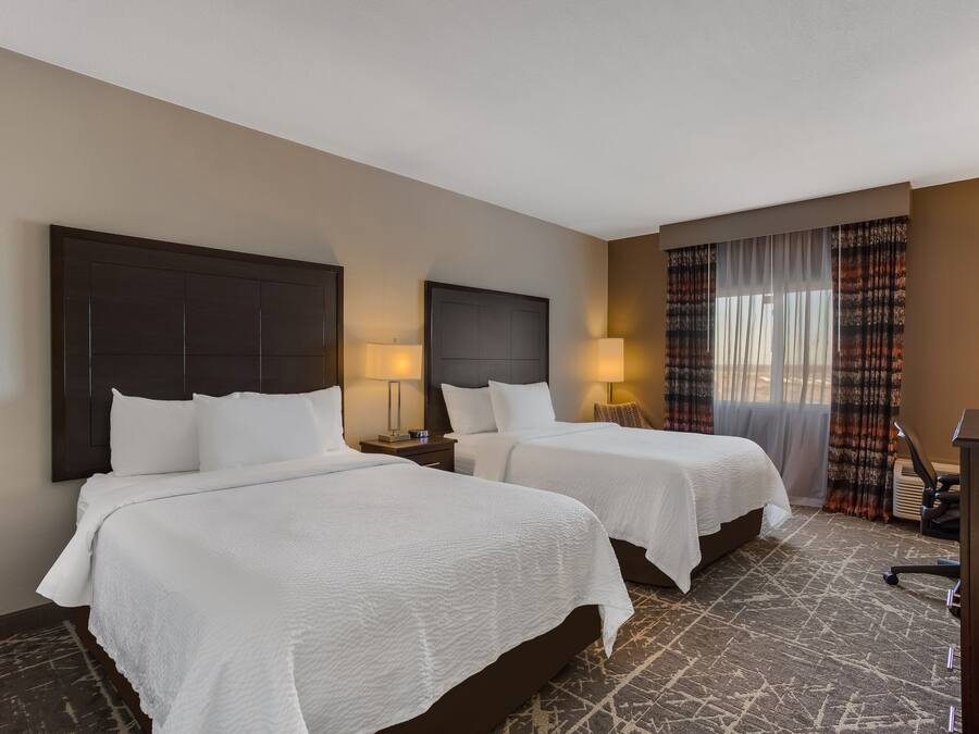 A hotel room with two beds, a desk, and a chair.