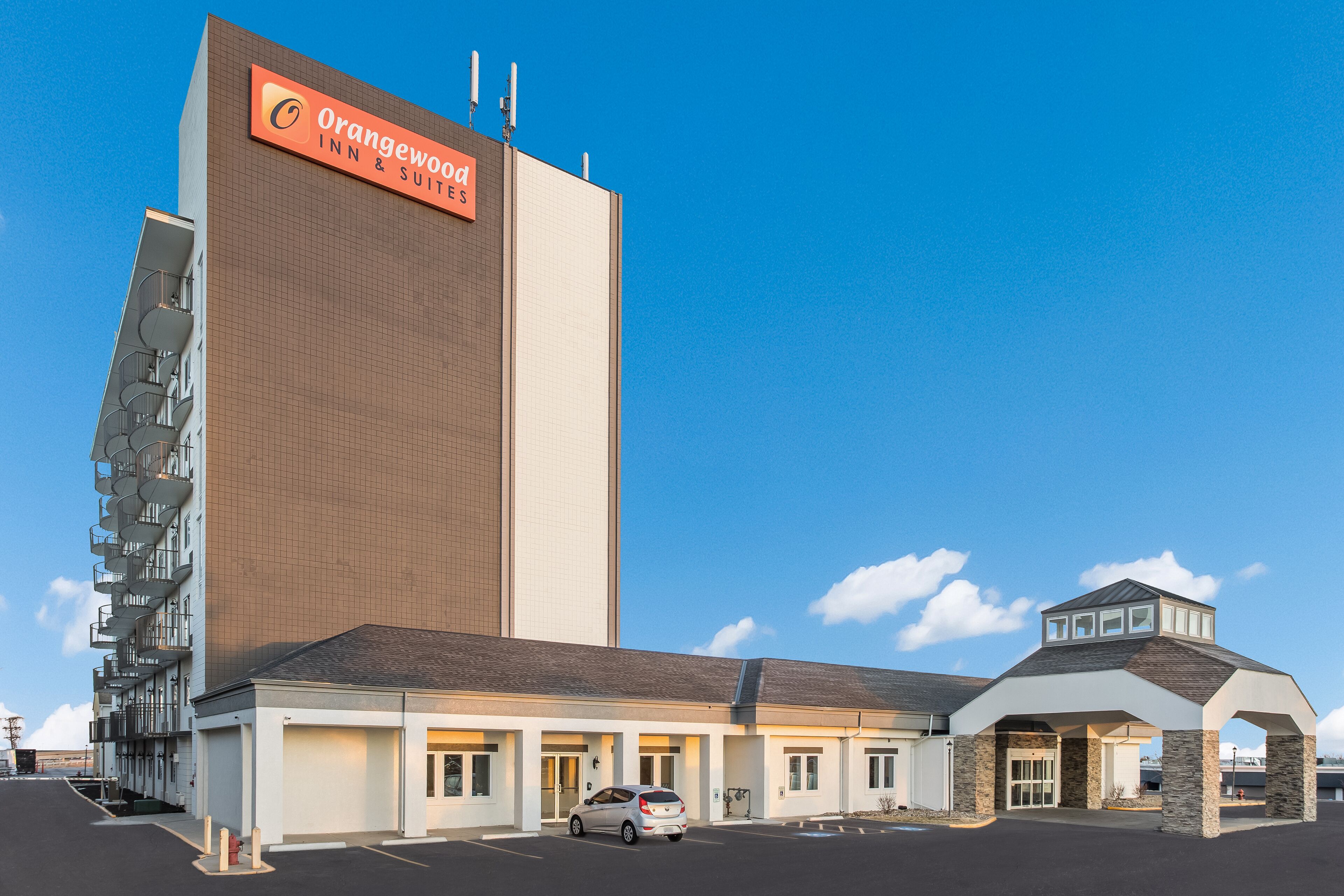 A hotel with a prominent Orangewood Inn & Suites sign, a parking lot, and a covered entrance.