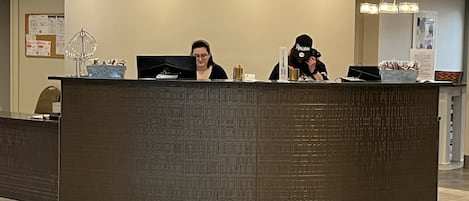 Un mostrador de recepción con dos empleados, una pared con diseño y un suelo de baldosas.