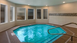 An indoor swimming pool with clear water, surrounded by beige tiled walls and windows with frosted glass.