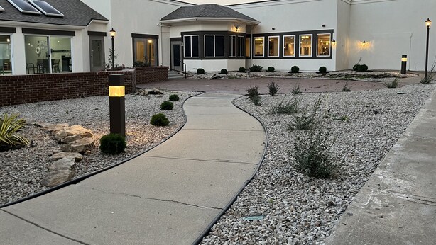 A modern building with a paved walkway, solar panels, and a landscaped garden with gravel and small shrubs.