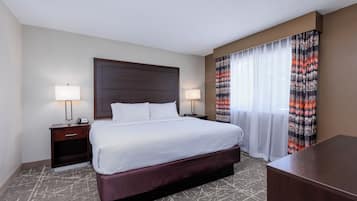 A hotel room with a large bed, two bedside tables with lamps, a wooden headboard, and a patterned curtain.