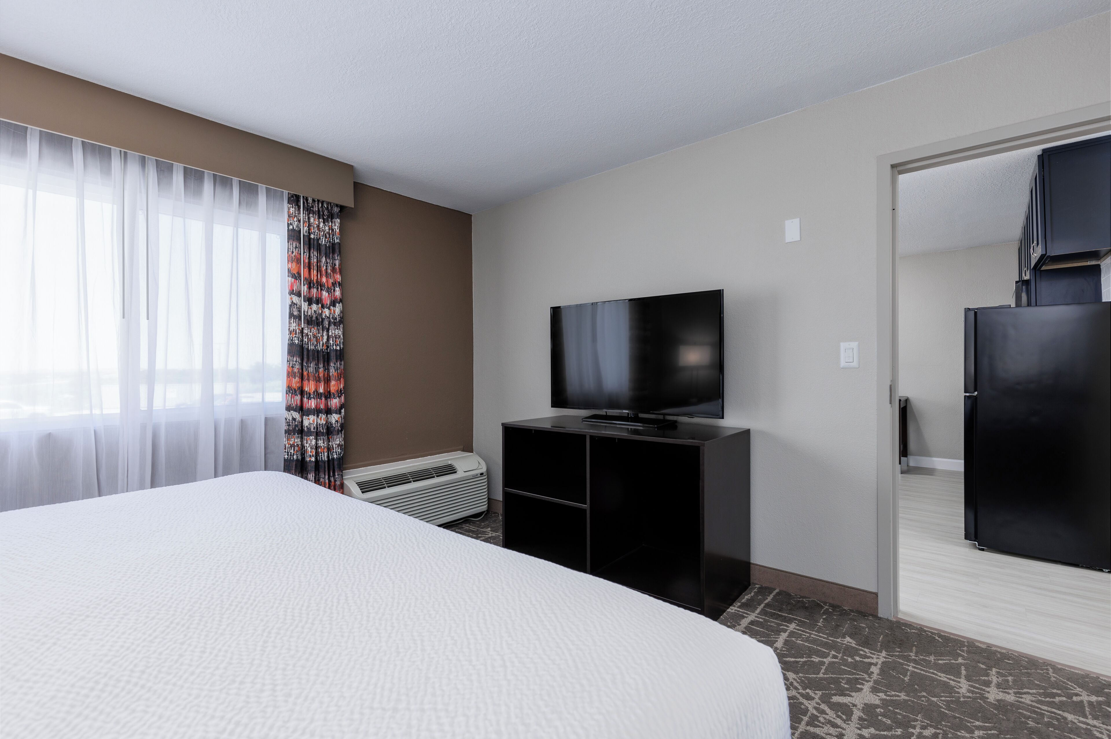 Habitación de hotel con una cama grande, televisión de pantalla plana, minibar y ventana con cortinas translúcidas.