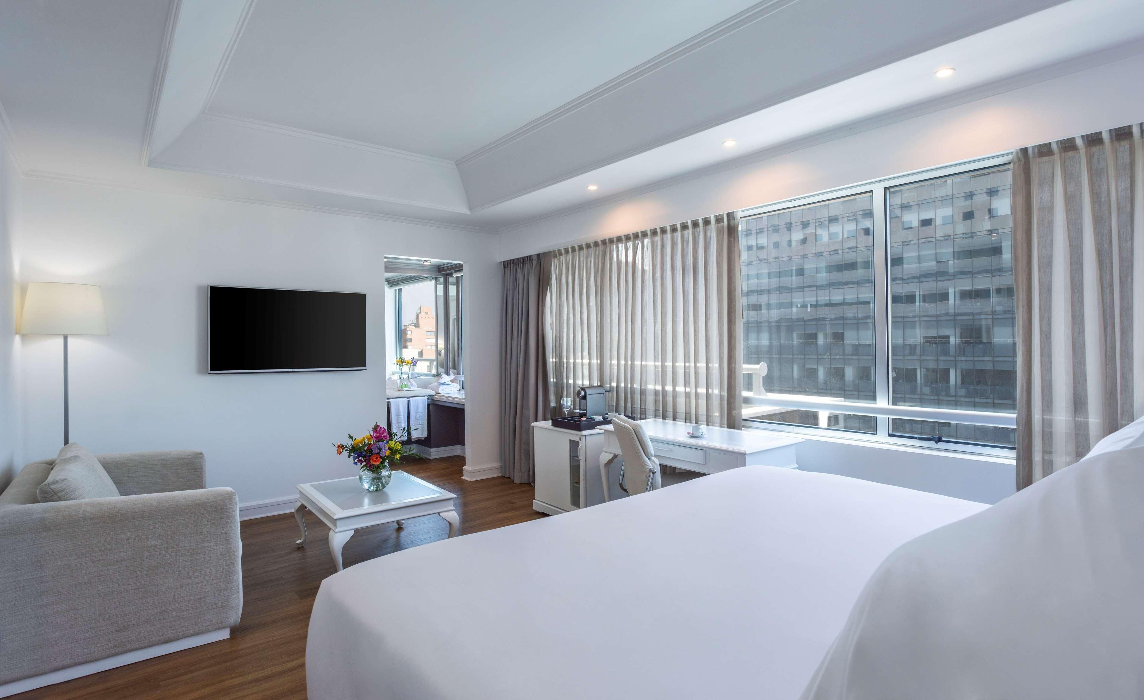 Une chambre d’hôtel équipée d’un lit, d’un bureau, d’une chaise, d’une télévision et offrant une vue sur le paysage urbain.