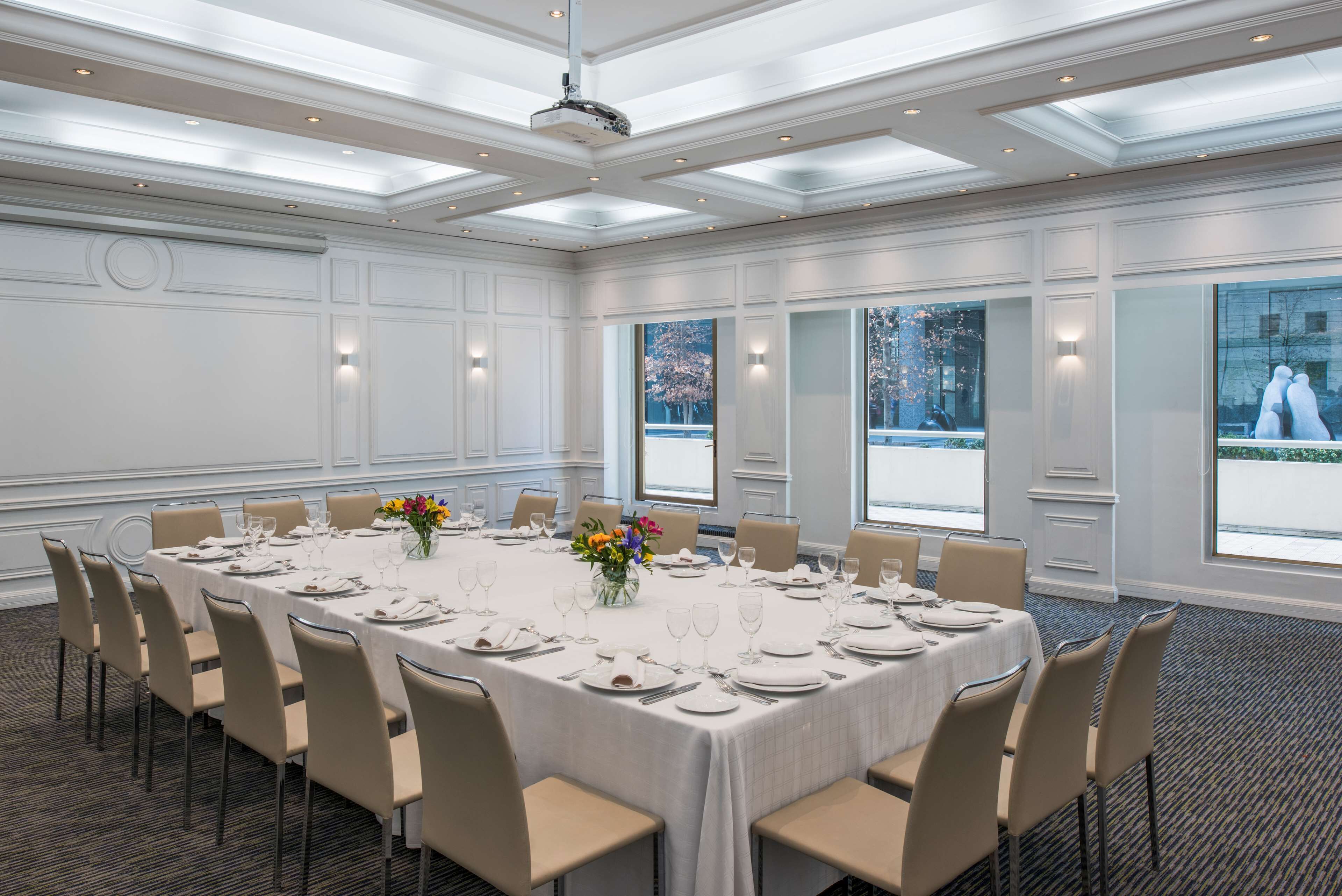 A conference room with a long table set for a meeting, large windows, and a modern ceiling design.
