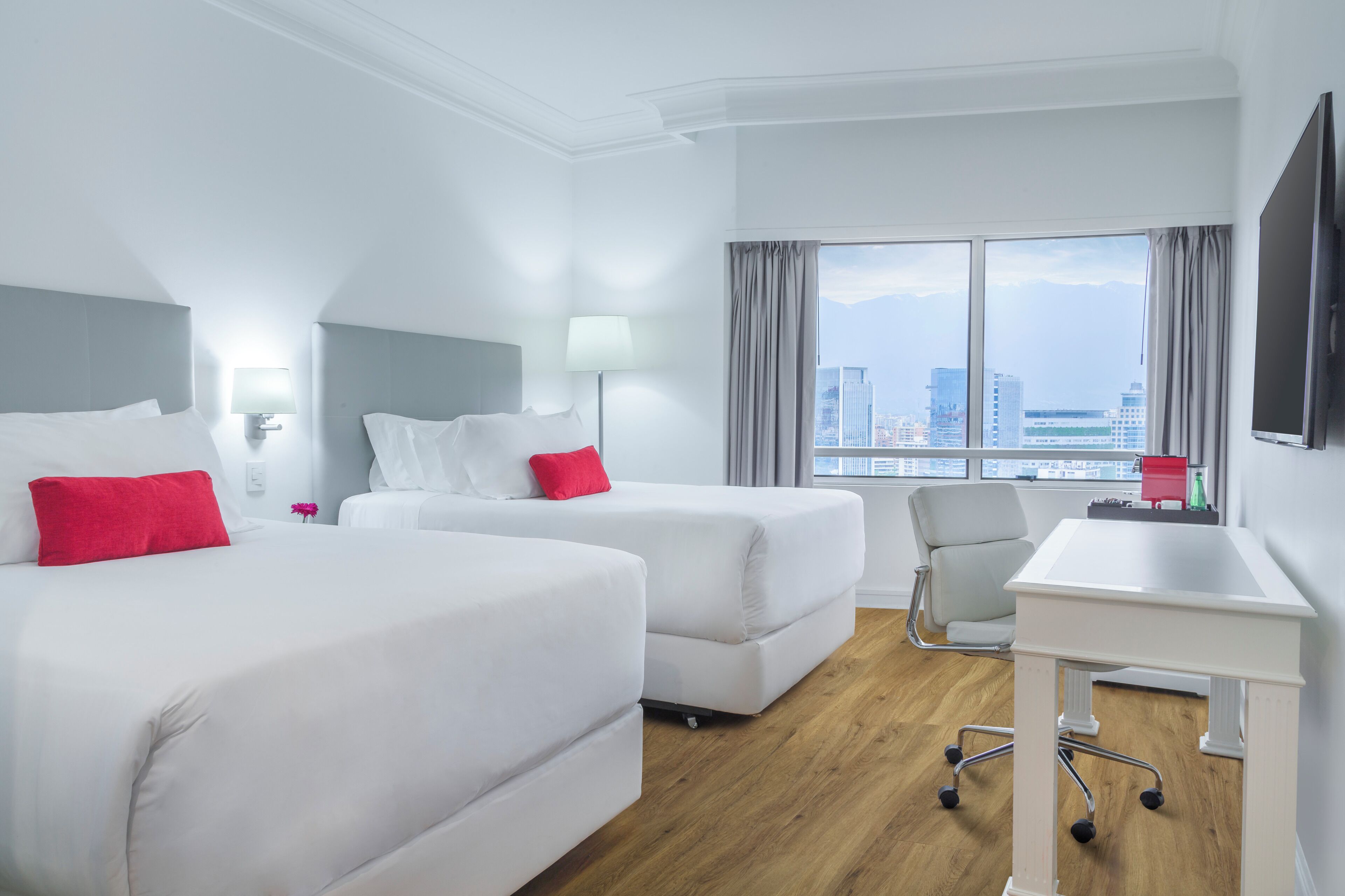 Une chambre d’hôtel avec deux lits, un bureau et une vue sur la ville.
