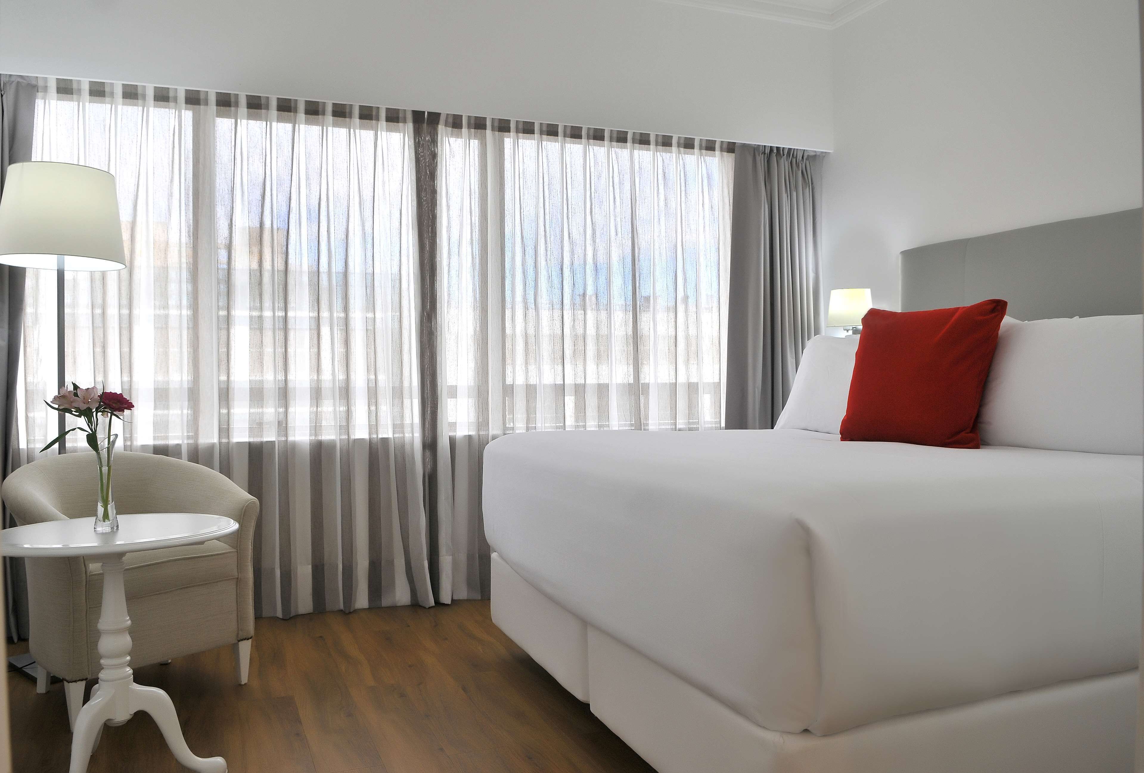 A hotel room with a large bed, a small table with a lamp, and a chair.