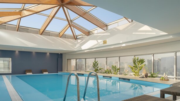 Una piscina interior amb aigua transparent de color blau, un sostre amb claraboines i vistes a la ciutat a través de grans finestres.
