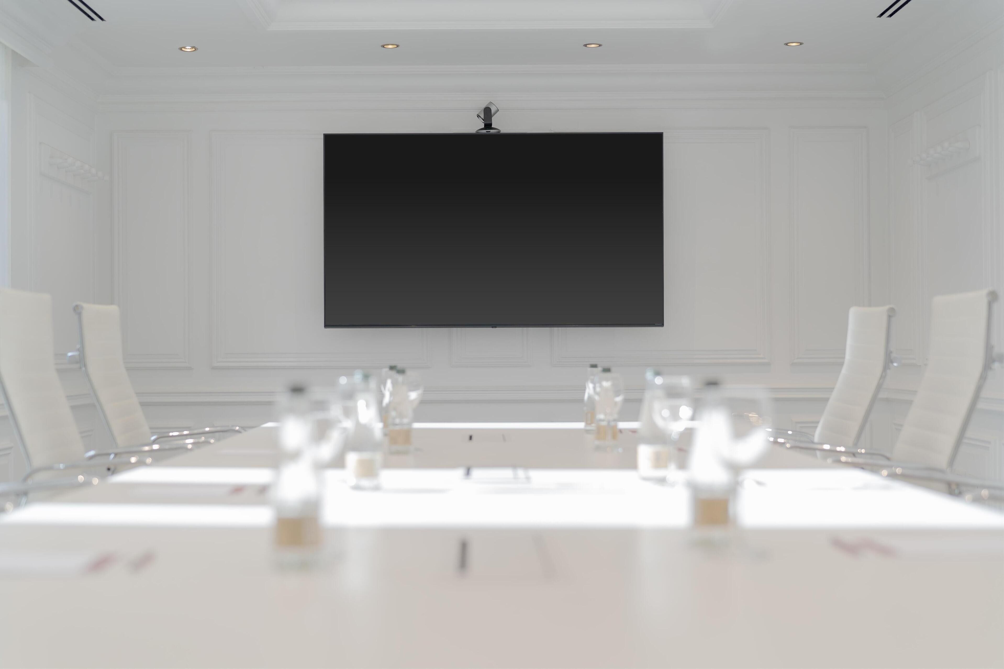 A conference room with a large table, white chairs, and a black screen on the wall.