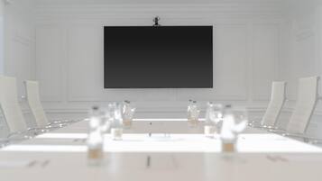 A conference room with a large table, white chairs, and a black screen on the wall.