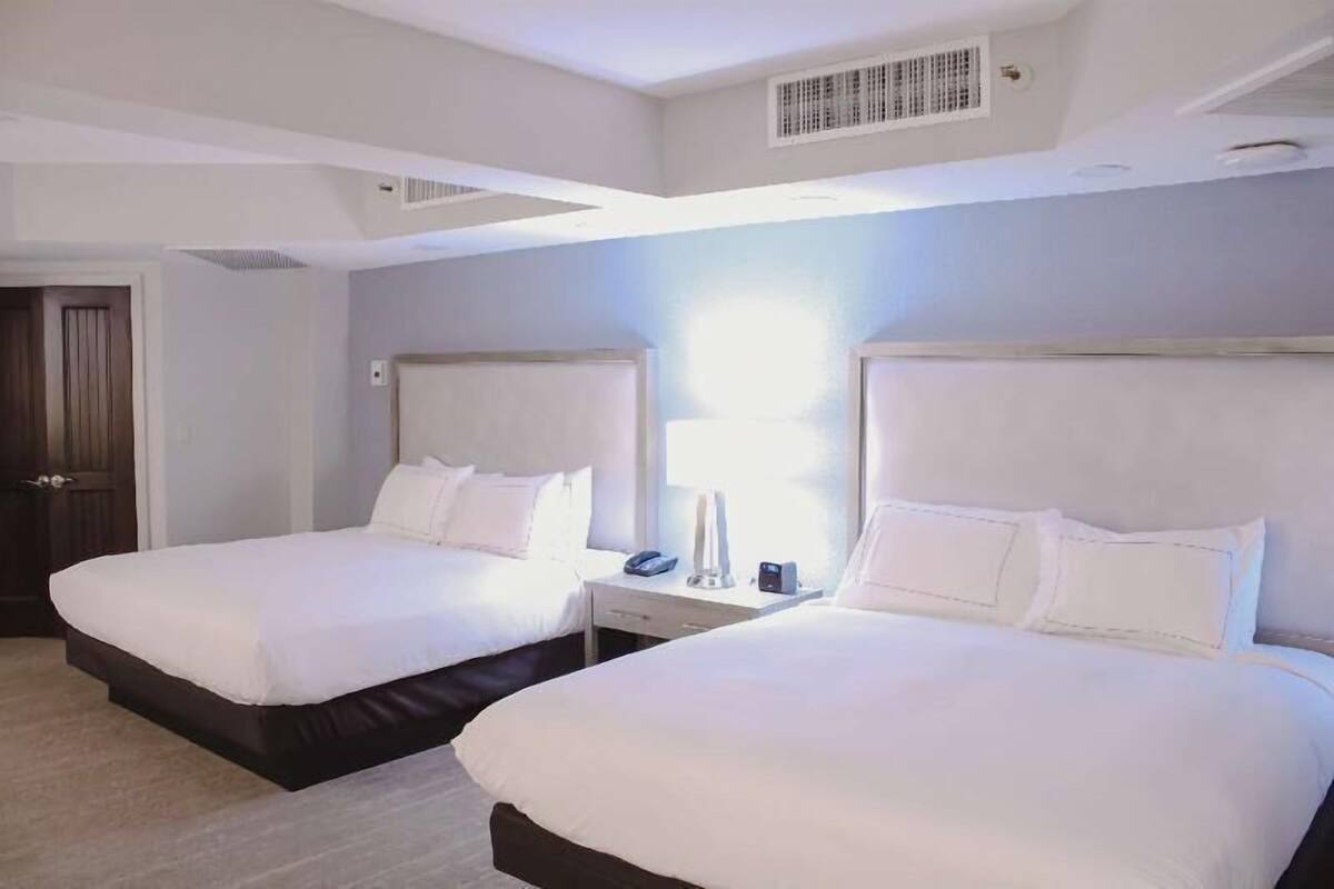 Une chambre d’hôtel avec deux lits, une table de chevet avec une lampe, un téléphone et une fenêtre.