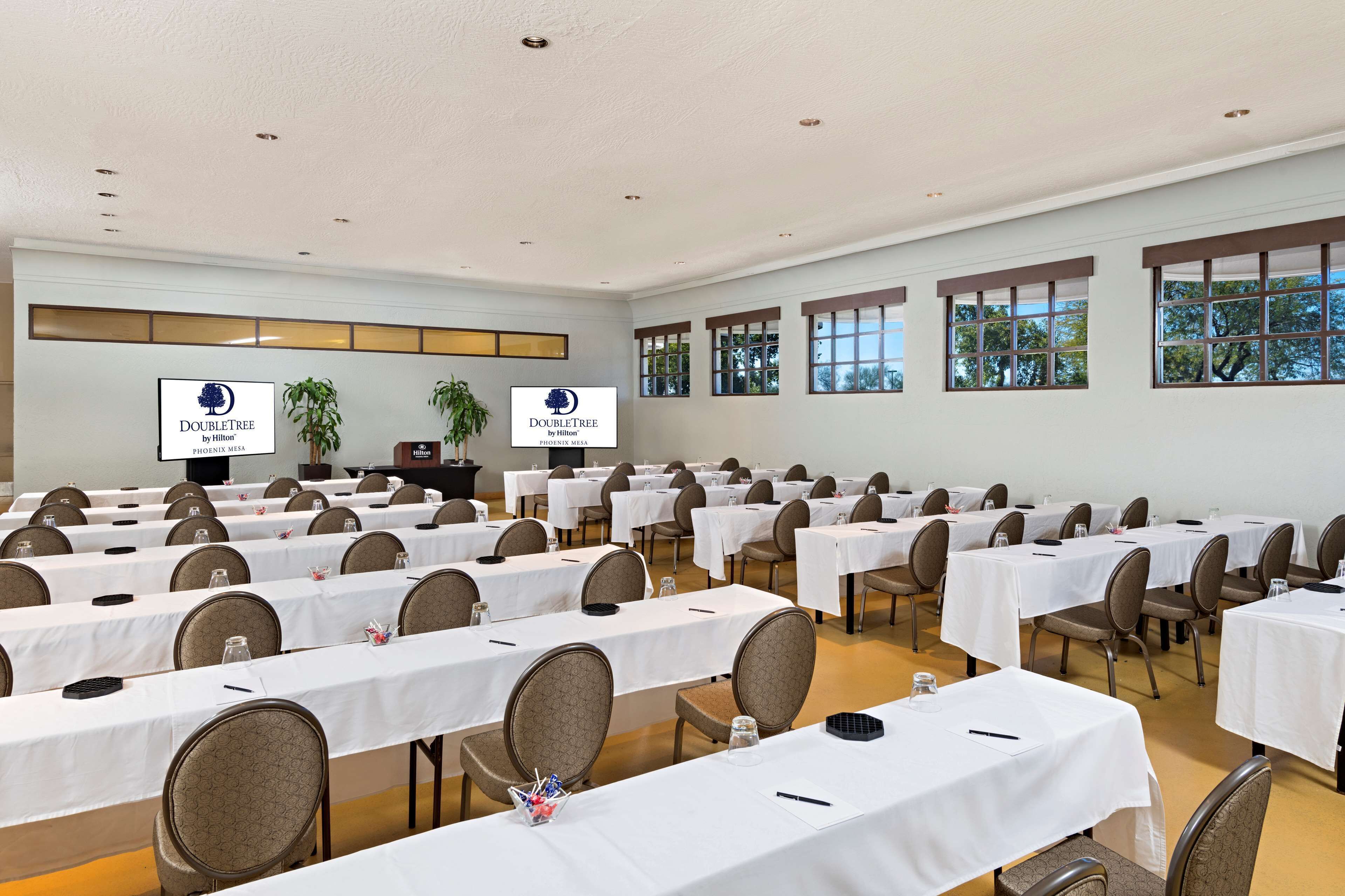 A conference room with multiple tables and chairs, white tablecloths, and a large screen displaying the DoubleTree logo.
