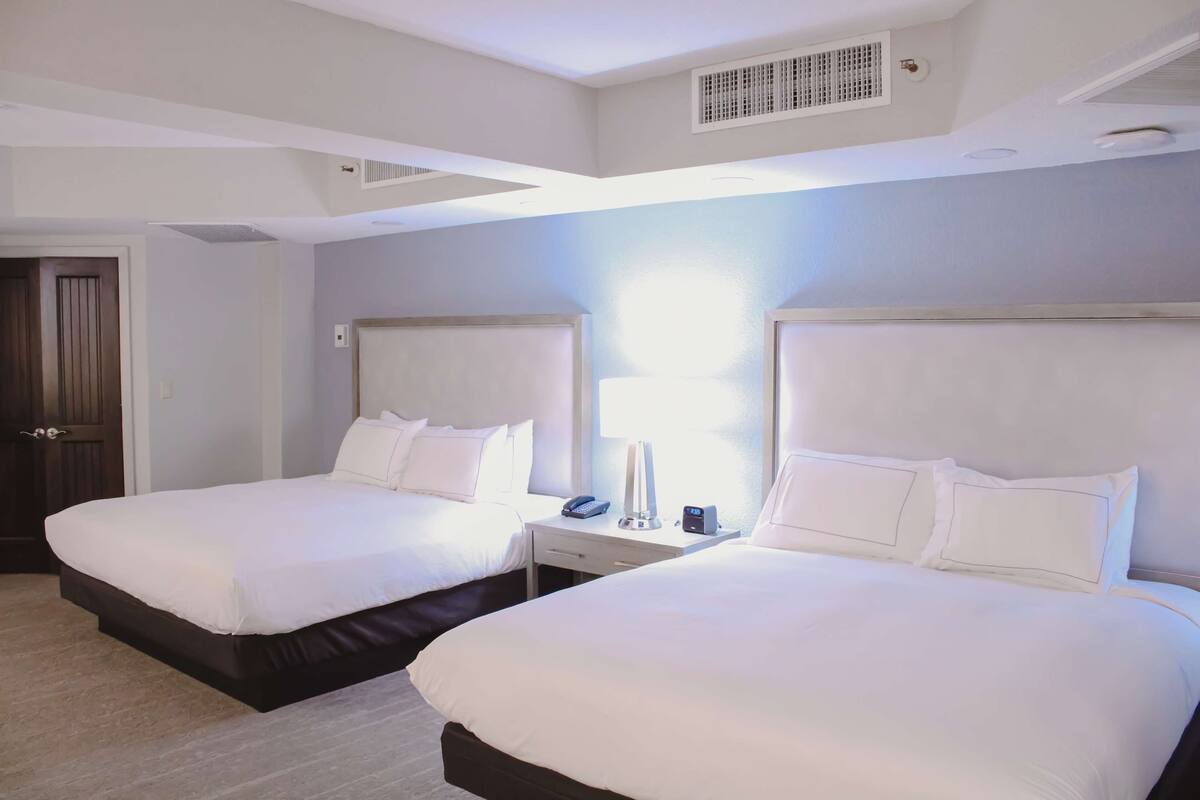 A hotel room with two beds, a bedside table with a lamp, and a phone.