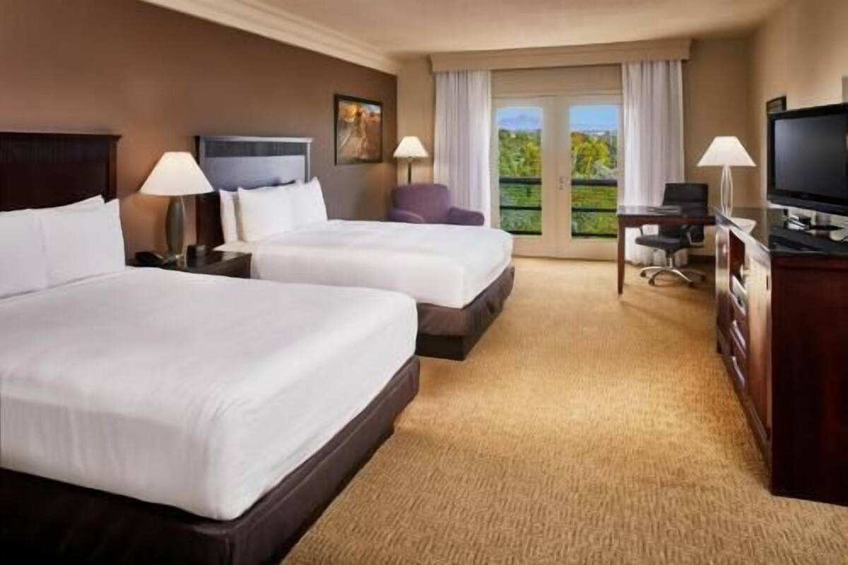 Une chambre d’hôtel avec deux lits, un bureau, une télévision et une vue sur l’extérieur.