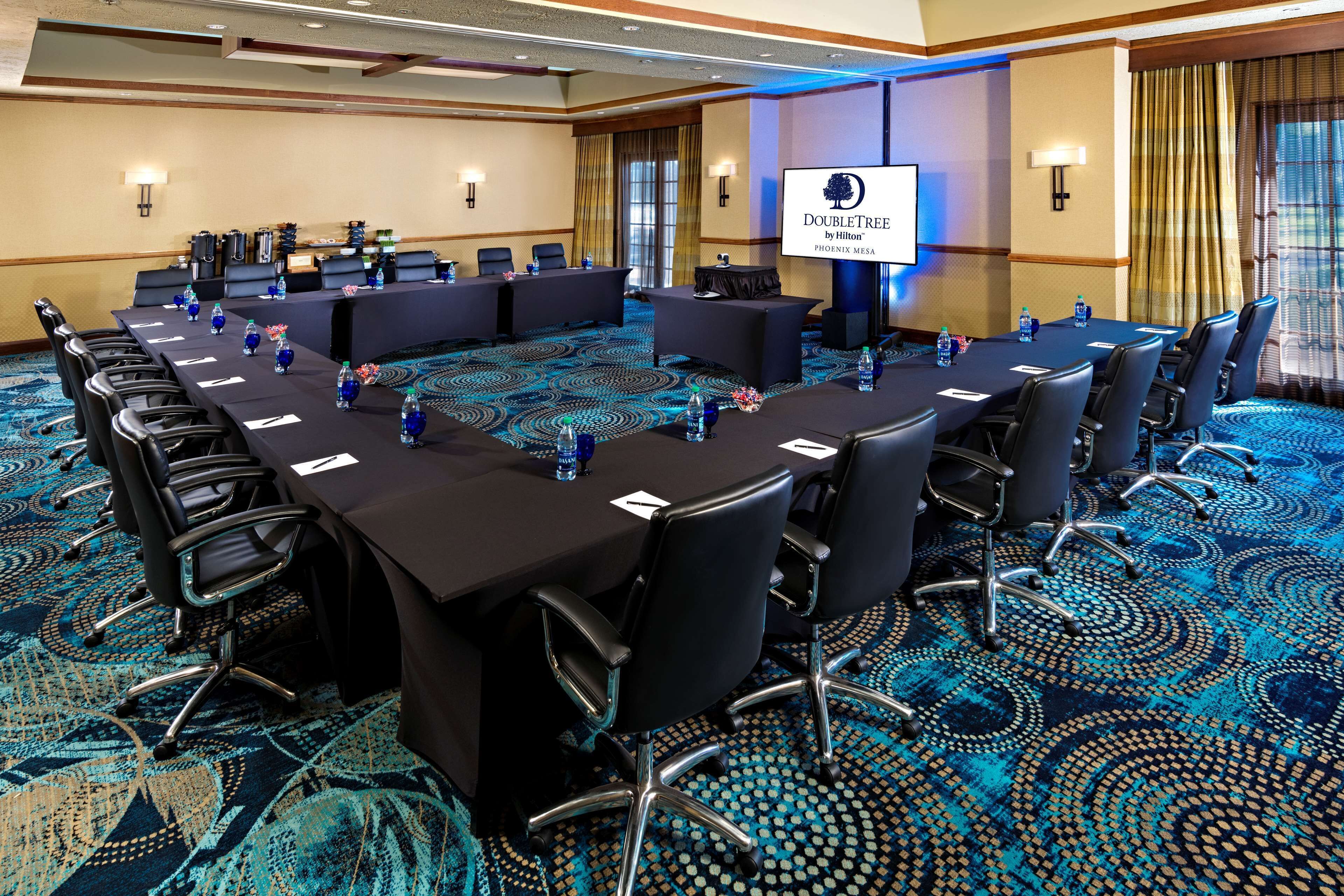 Een vergaderruimte met een lange tafel, meerdere stoelen en een scherm waarop het logo van DoubleTree by Hilton wordt getoond.