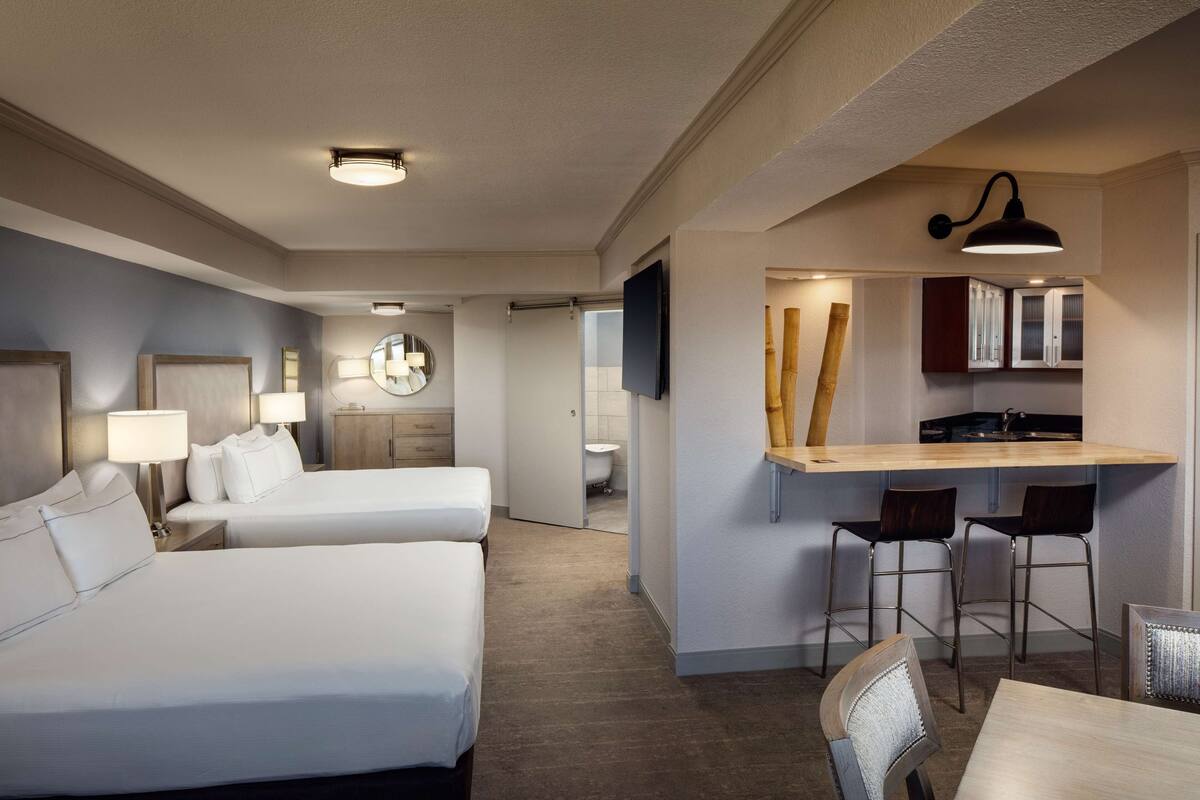 A hotel room with two beds, a desk with chairs, a mirror, and a TV.