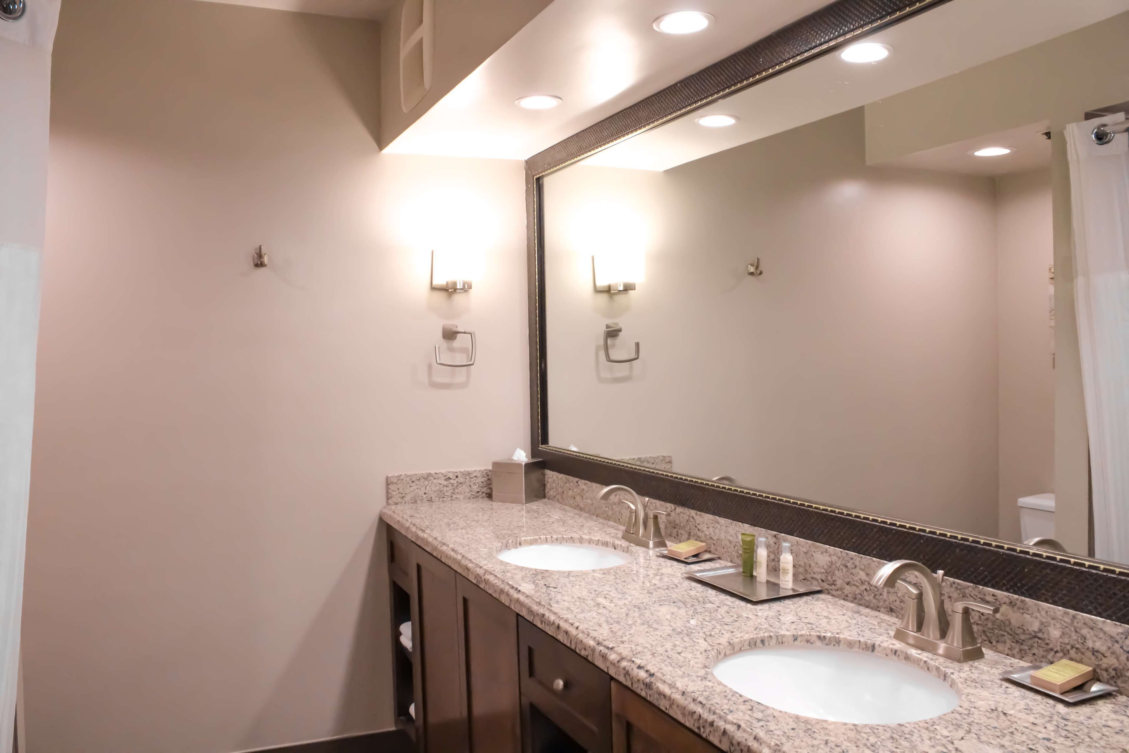 Un baño con dos lavamanos, un espejo grande y luces empotradas.