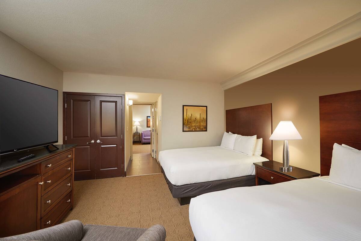 A hotel room with two beds, a TV, a dresser, and a lamp.