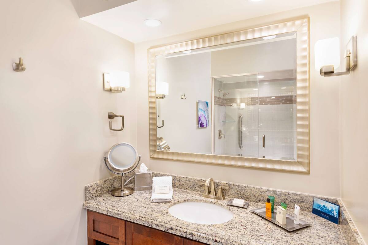 A bathroom with a large mirror, a sink, a vanity, and a shower.