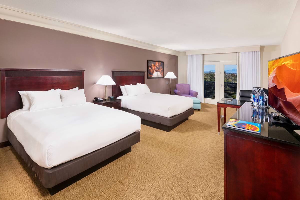 A hotel room with two beds, a desk with a computer, a chair, and a TV.