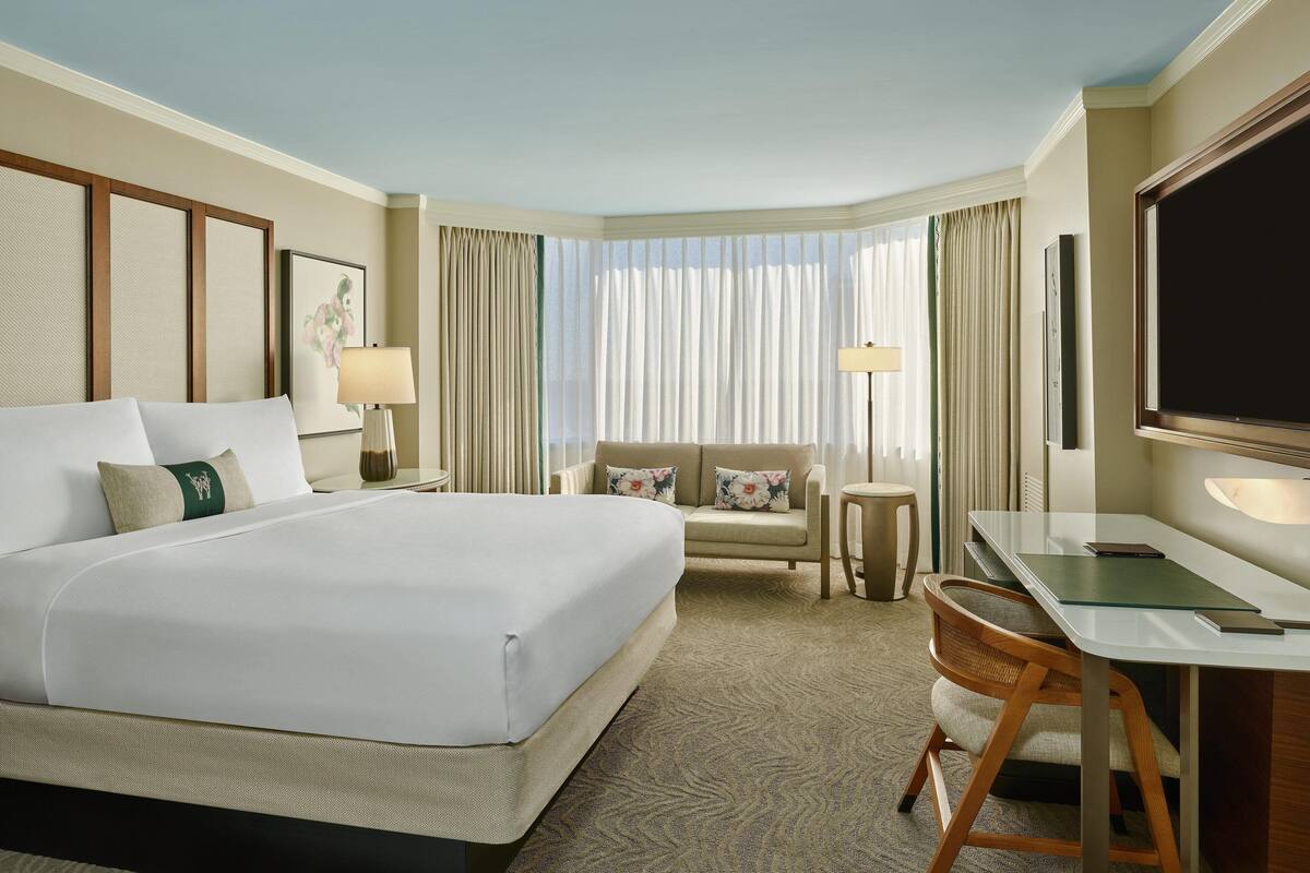 A hotel room with a large bed, a desk, a chair, and a sofa.