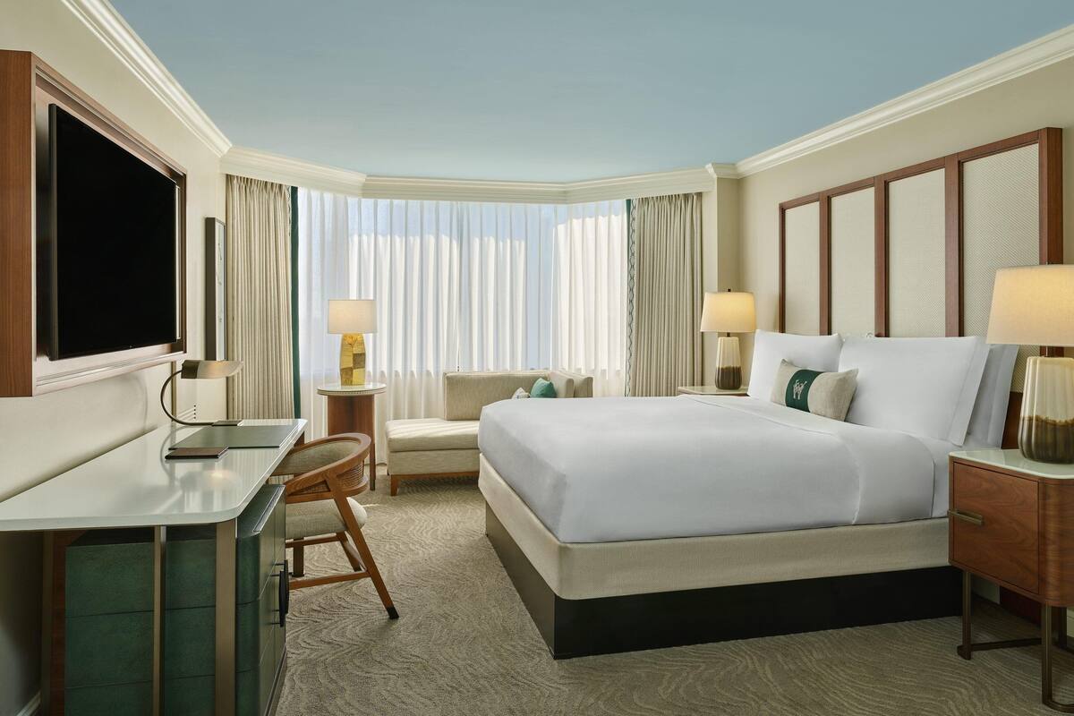A hotel room with a large bed, a desk, a chair, a TV, and two bedside lamps.